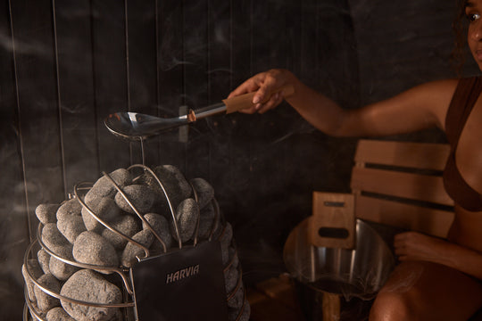 Woman pouring water on stones in Lewisburg Onyx Outdoor Sauna
